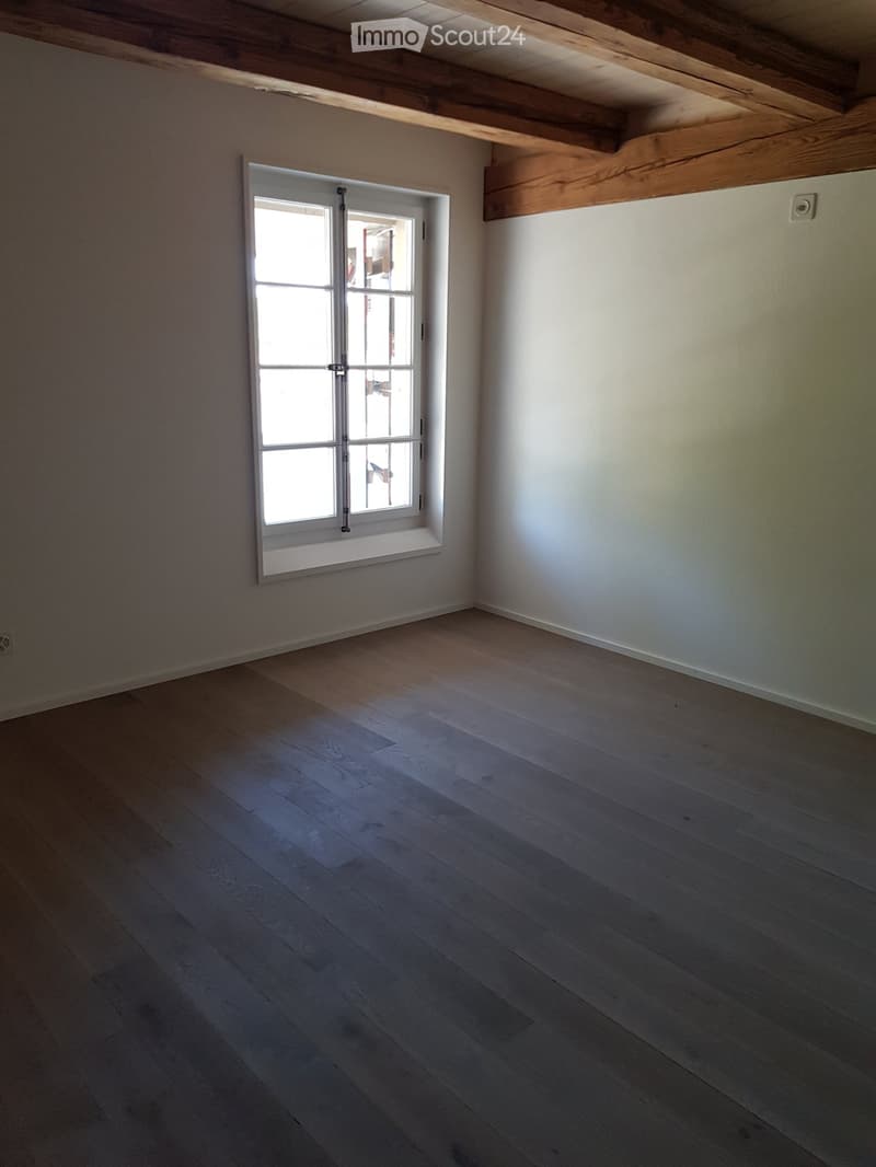 Empty room with wooden flooring, white walls, and a single window with white frame and glass panes.