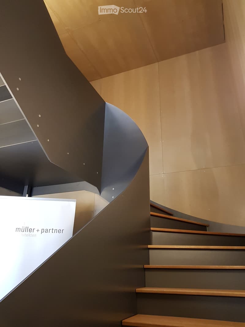 Modern staircase with wooden steps and dark metal railings, featuring a sleek, angular design and warm-toned walls.