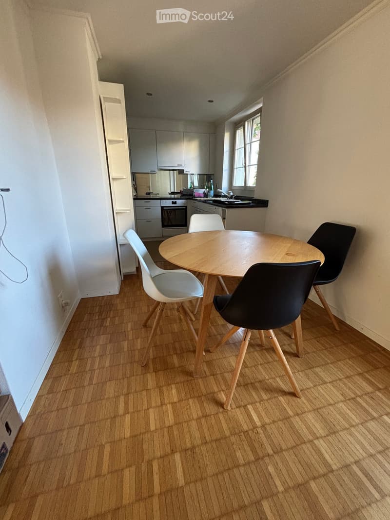 A modern, open-plan kitchen and dining area with light wooden flooring, white cabinets, and a round wooden dining table with four chairs.