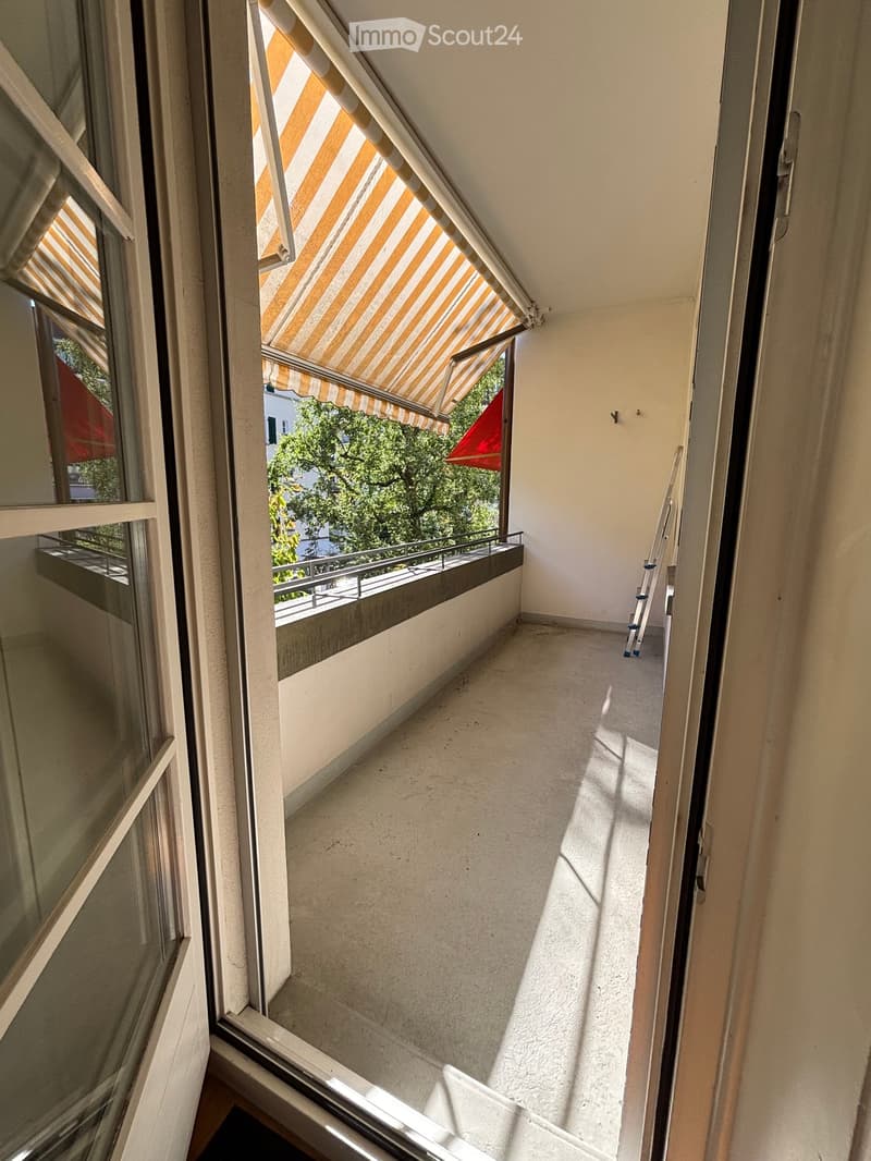 Balcony with striped awning, metal railing, and view of greenery outside.