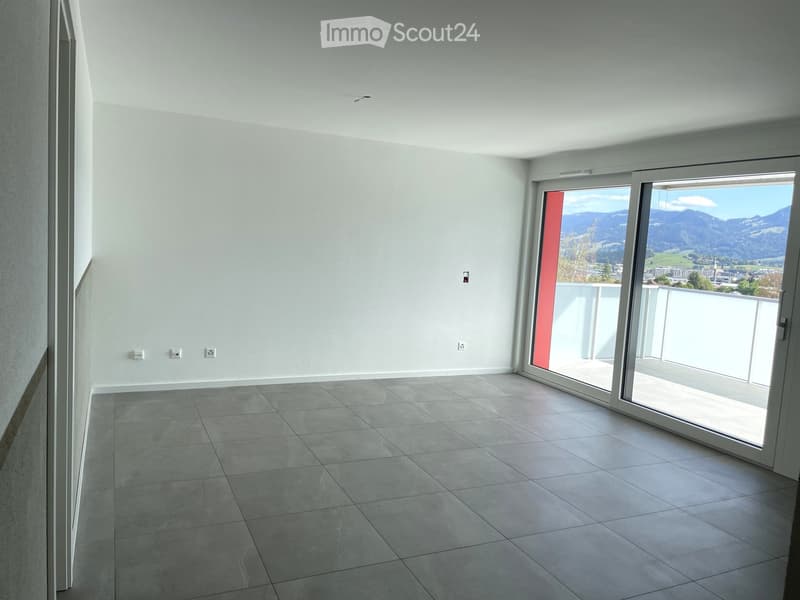 Empty room with tiled floor, white walls, and large sliding glass door leading to a balcony with scenic mountain view.