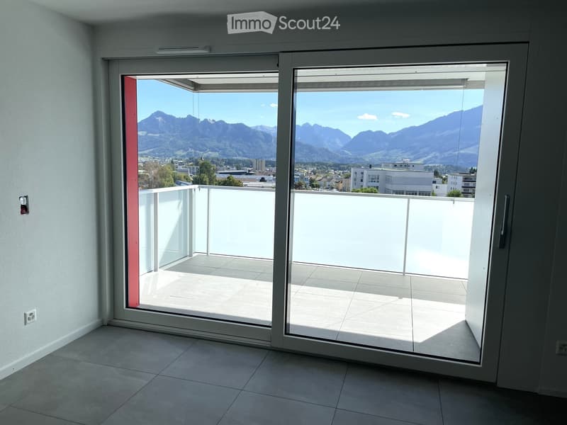 Empty room with large sliding glass doors opening to a balcony, offering a scenic mountain view.