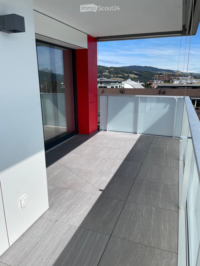 Modern balcony with grey tiled floor, white walls, glass railing, and scenic mountain view.