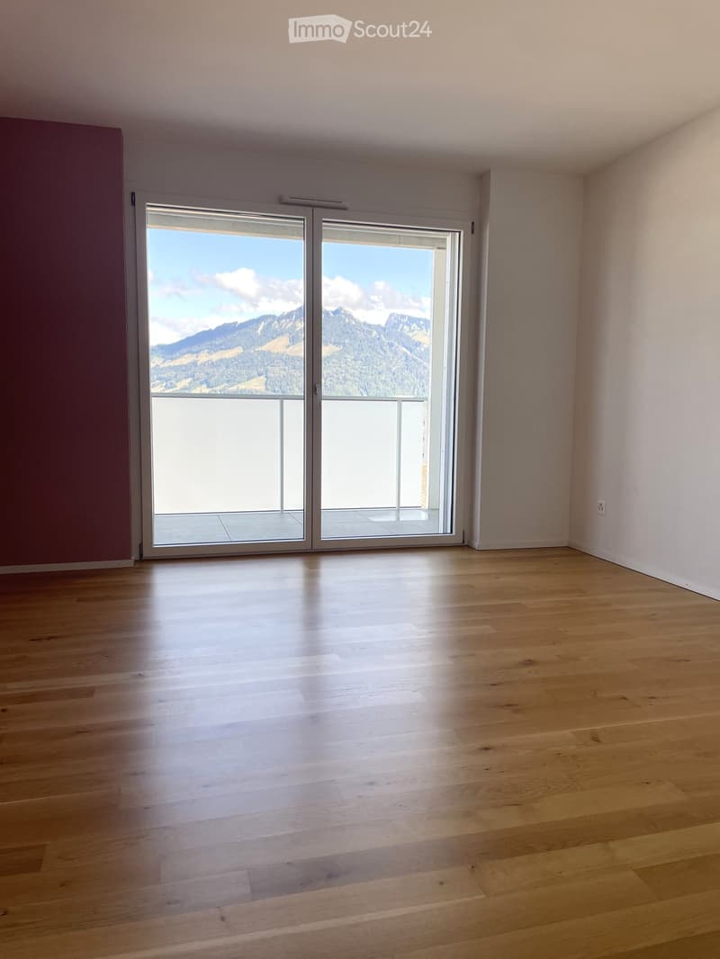 Empty room with wooden flooring and large sliding glass doors leading to a balcony with a scenic mountain view.