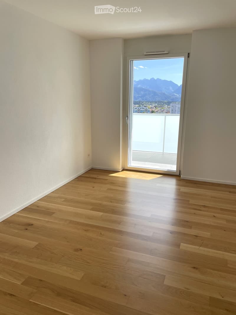 Empty room with light wooden flooring, white walls, and a large sliding glass door leading to a balcony with a scenic mountain view.