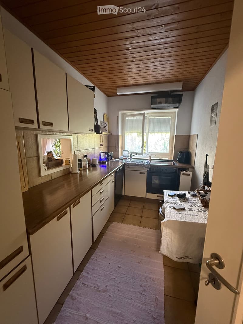 Modern kitchen with white cabinets, wooden countertops, and stainless steel appliances. Features a sink, oven, dishwasher, and a small table with a tablecloth.