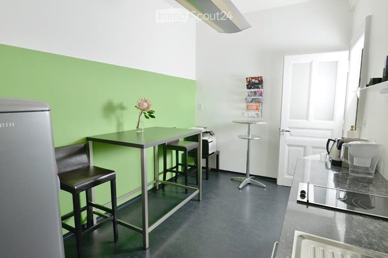 green and white walls, small dining table, metal stools, refrigerator, microwave, sink, electric kettle, coffee machine, toaster, countertop