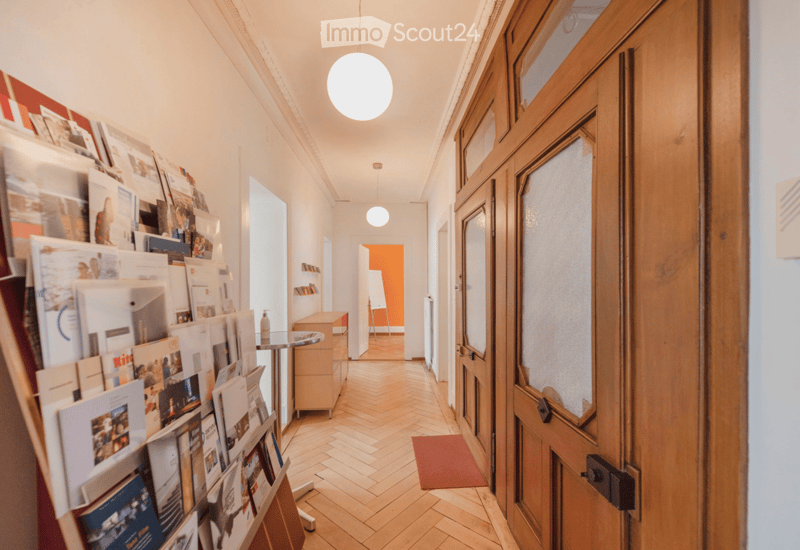corridor, parquet flooring, wooden doors, bulletin board with photos and brochures, cabinet, round table with a bottle