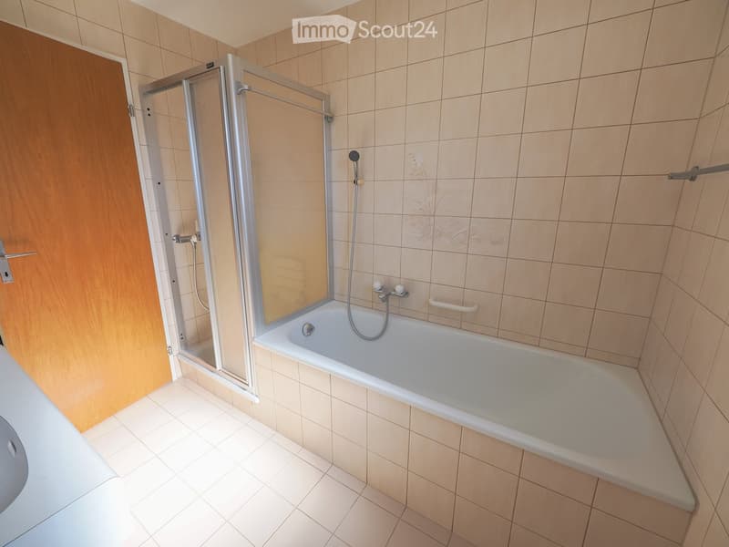 Modern bathroom with a bathtub, glass-enclosed shower, tiled walls, and a wooden door.