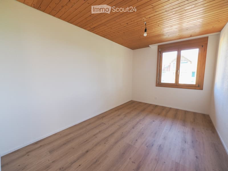 Empty room with wooden flooring, white walls, and a wooden ceiling. Features a single window with wooden frame and a ceiling light fixture.
