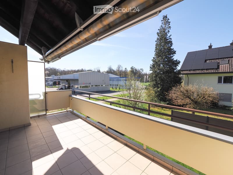 Balcony with tiled floor, metal railing, and a view of a green area with trees and a building in the background.