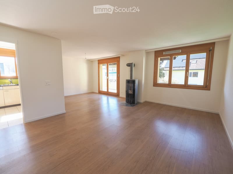 Empty room with wooden flooring, white walls, large windows, and a fireplace in the center.