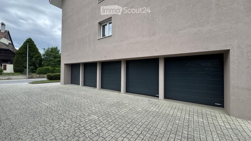 Modern two-story building with four dark garage doors and a single window on the upper level.