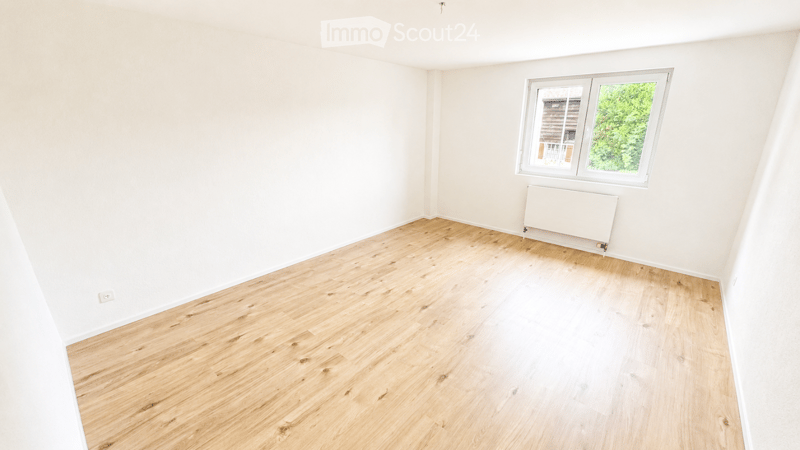 Empty room with light wooden flooring and white walls, featuring a single window with a radiator below it.