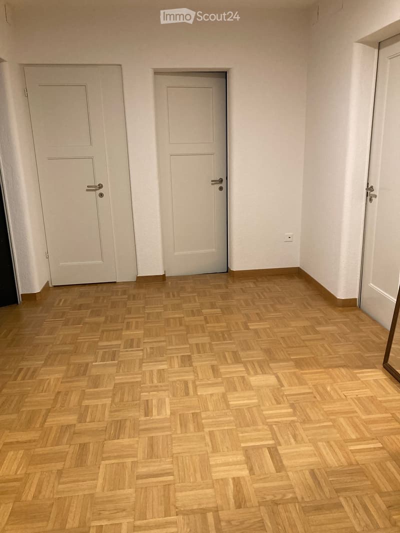Empty hallway with wooden herringbone flooring, white walls, and two closed doors.