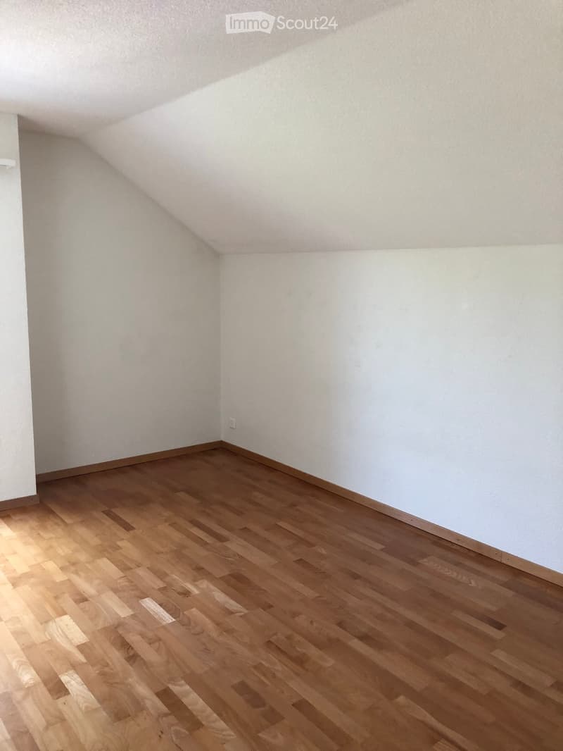 Empty room with wooden flooring and white walls, featuring a slanted ceiling typical of an attic space.