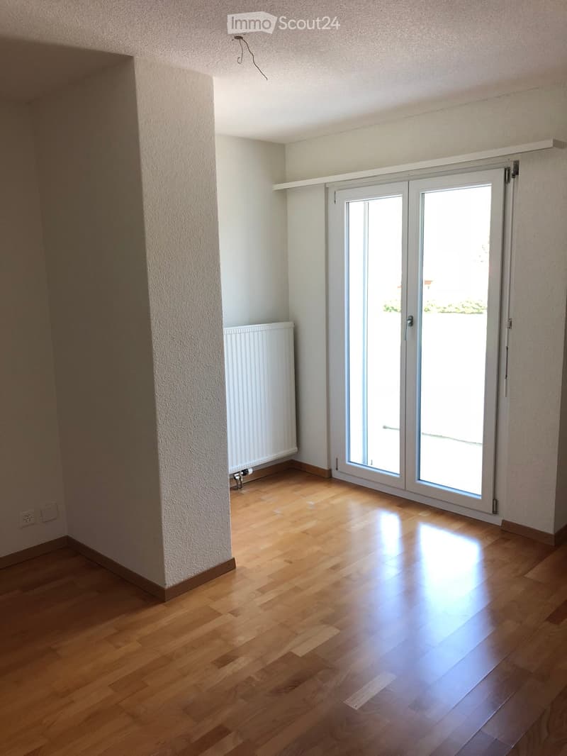 Empty room with wooden flooring, white walls, and a large sliding glass door leading to a balcony.