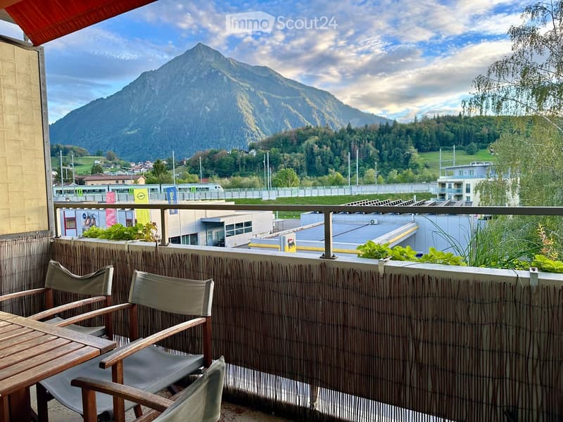 Balcony with wooden table and chairs, overlooking a mountain range and town below.