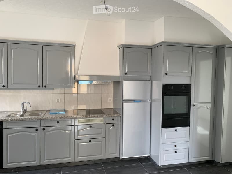 Modern kitchen with grey cabinets, stainless steel sink, refrigerator, and oven. Granite countertop and tiled backsplash.