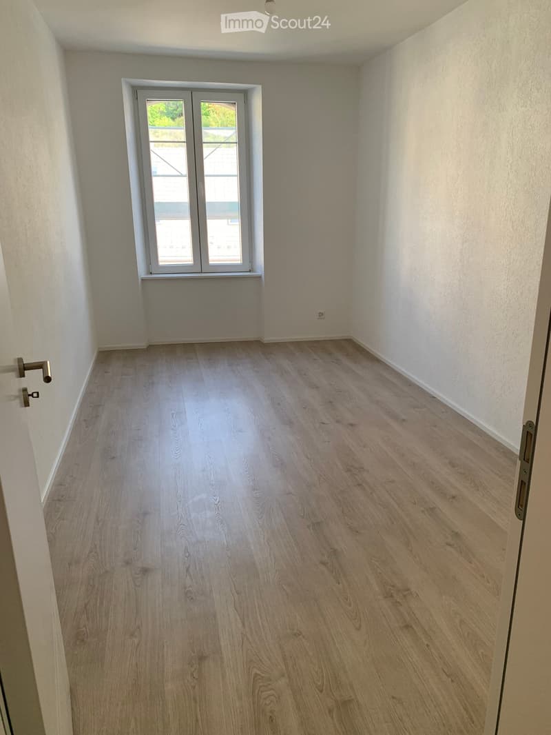 Empty room with light wooden flooring, white walls, and a window with a view of a balcony area.
