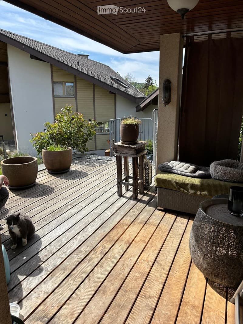 Wooden deck with a cat, small stool, table, cup, potted plants, and a small sofa.