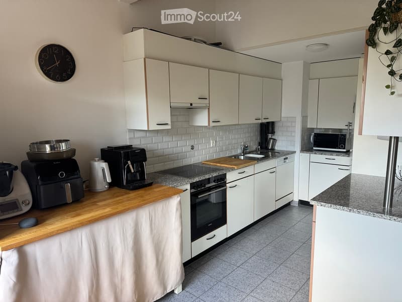 Modern kitchen with white cabinets, granite countertops, stainless steel appliances, and a wooden cutting board on the counter.