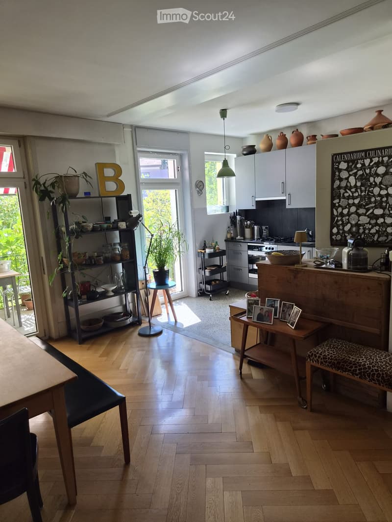Open-plan kitchen and dining area with wooden flooring, modern cabinets, and various furniture including a dining table, chairs, and a stool.