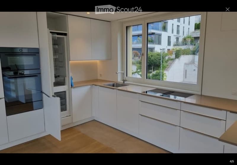 Modern kitchen with white cabinets, wooden countertops, stainless steel appliances, and large windows offering a city view.