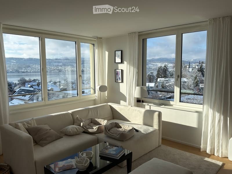Bright living room with large windows offering a scenic view, featuring a white sectional sofa, coffee table, and lamps.