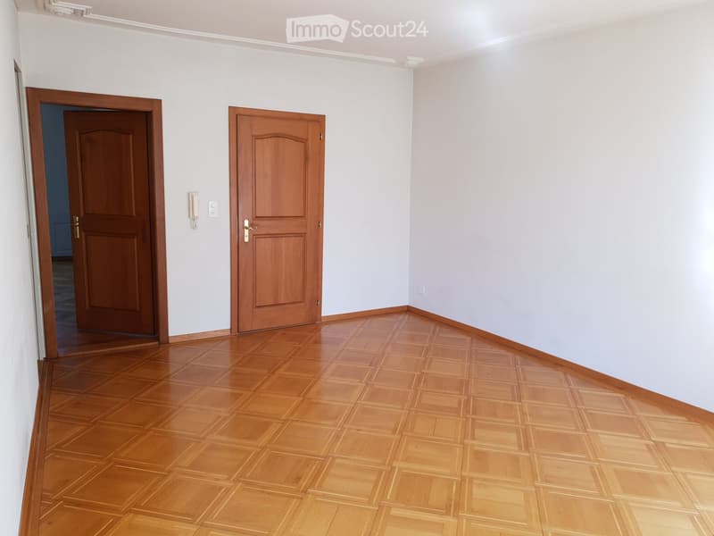 Empty hallway with wooden flooring and two wooden doors, light grey walls, and a telephone on the wall.