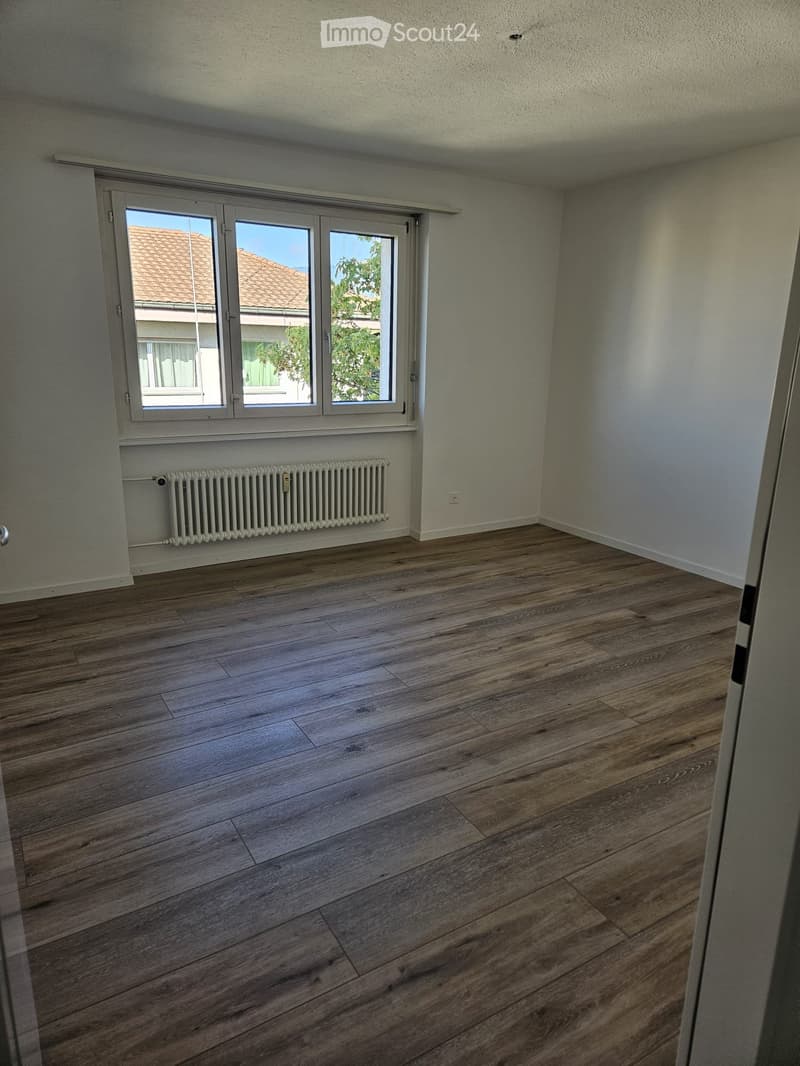 Empty room with wooden flooring, white walls, and a window with a radiator below it.