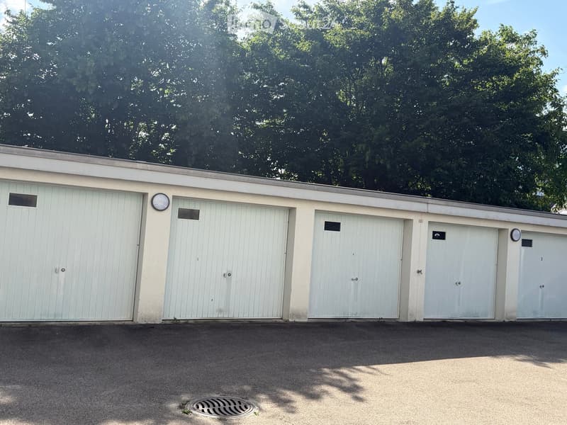 Four white garage doors on a single-story building with a flat roof, surrounded by trees.