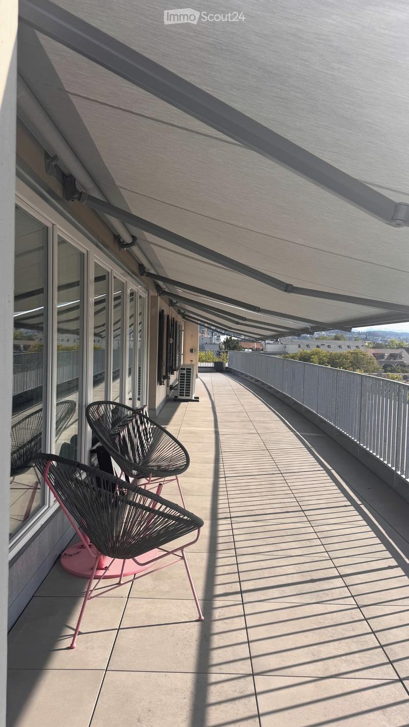 Balcony with modern chairs, covered roof, and cityscape view.