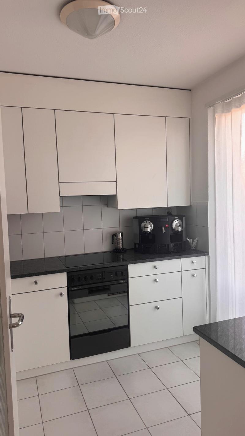 Modern kitchen with white cabinets, black countertop, and stainless steel appliances including an oven and coffee machine.