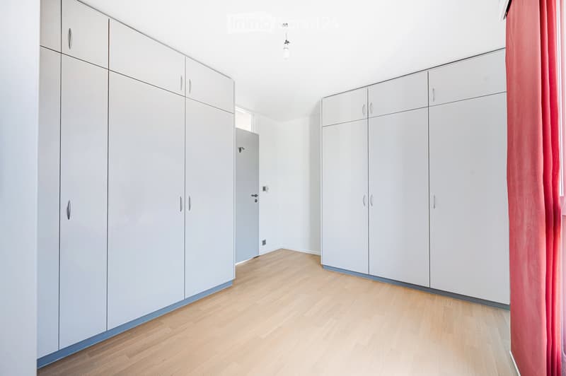 Empty room with light grey built-in wardrobes, wooden flooring, and a red curtain on the right side.