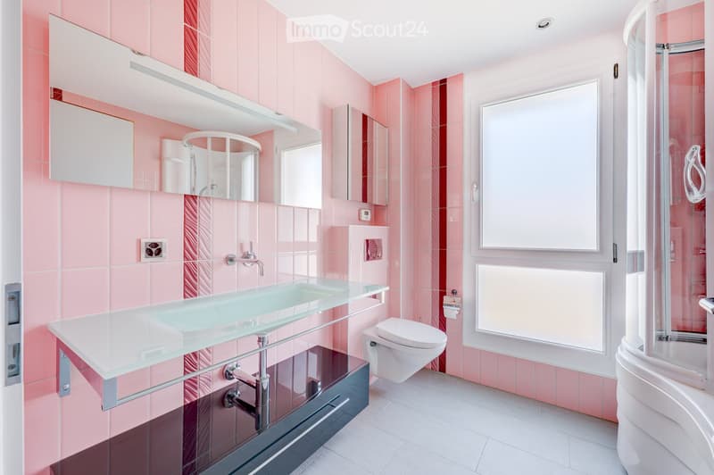 Modern bathroom with pink tiles, a glass sink, a large mirror, a toilet, and a shower area with a glass enclosure.