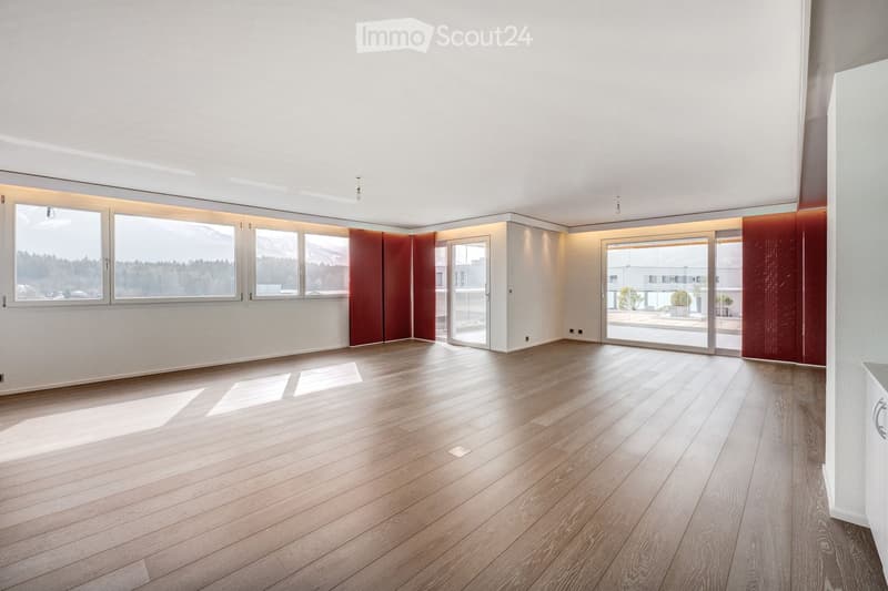Empty room with wooden flooring, large windows, and sliding glass doors leading to a balcony.