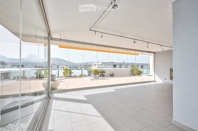 Modern balcony with large glass walls, tiled floor, and a view of the surrounding landscape and buildings.