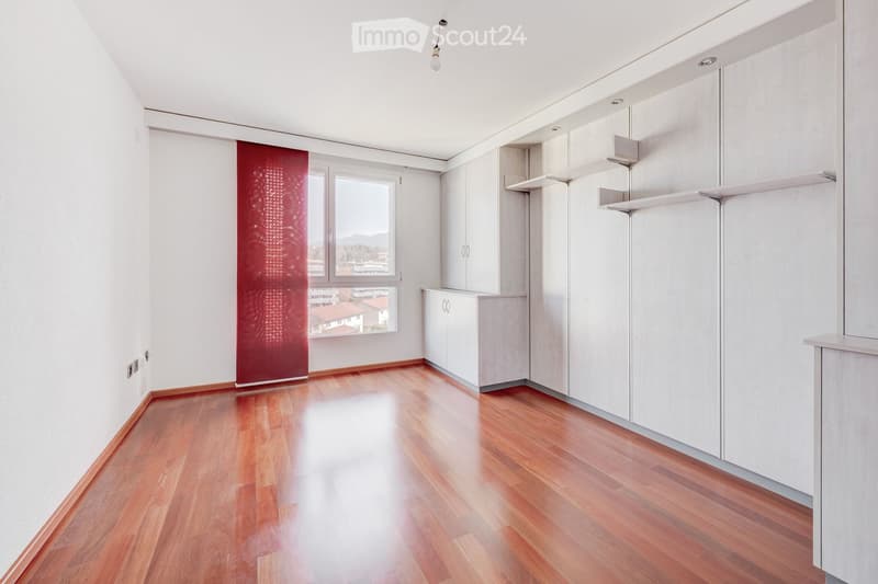 Empty room with wooden flooring, white walls, built-in white cabinets, and large windows offering a view of the outside.
