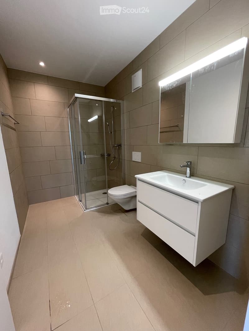 modern bathroom with a shower, a white vanity, a toilet, a towel rack, and tiled walls and floors