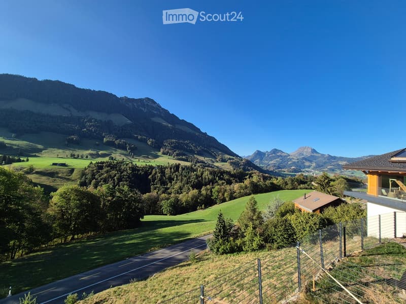A modern house with a balcony and a view of green fields and mountains in the background.