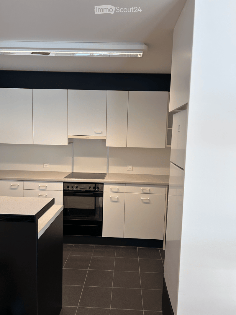 Modern kitchen with white cabinets, black oven, and dark tiled floor.