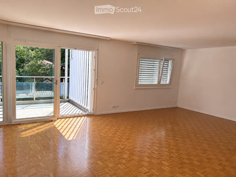 Empty room with wooden parquet flooring, large sliding glass doors leading to a balcony, and a window with blinds.