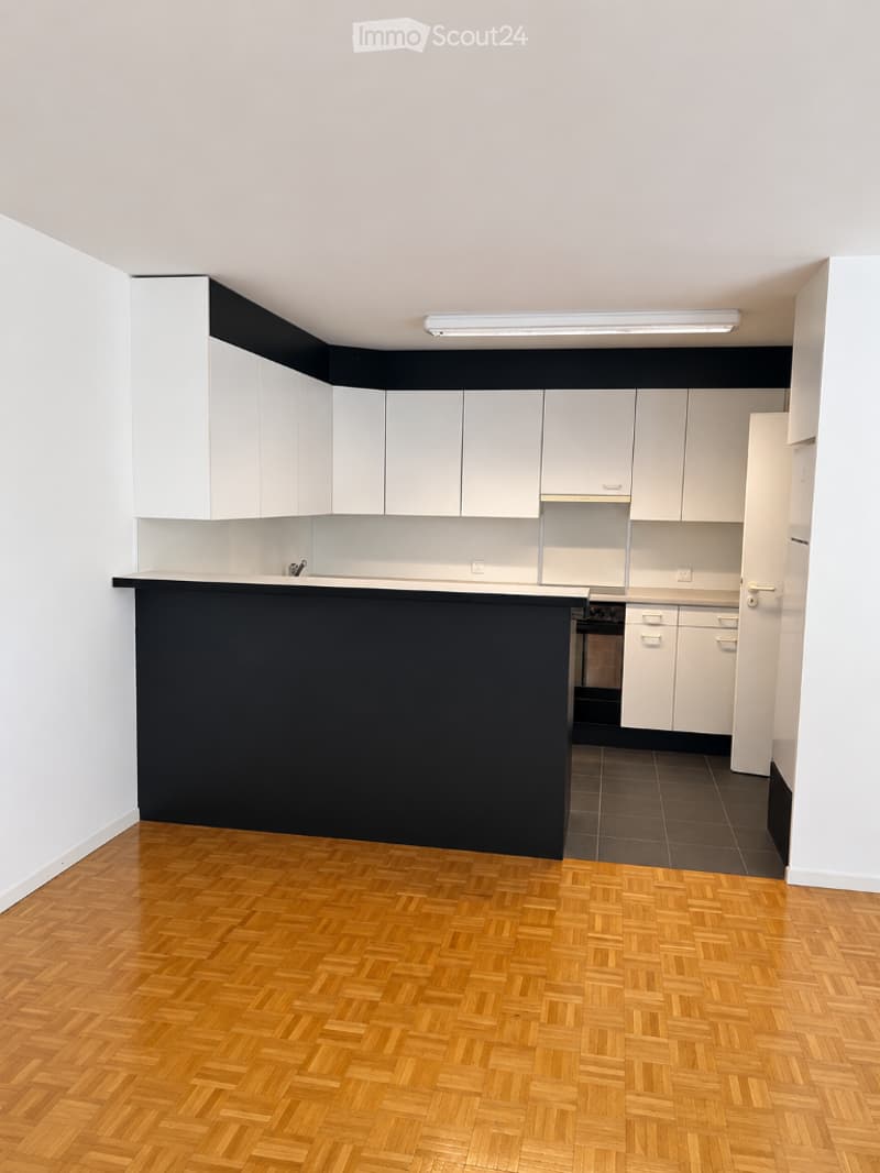 Empty kitchen with white cabinets, black countertop, and wooden flooring.