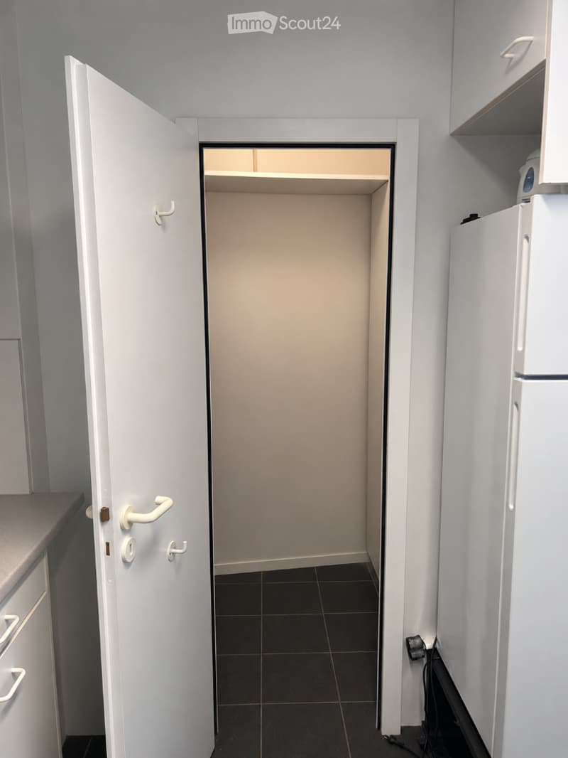 Empty room with white walls, black tiled floor, and a partially open door leading to another room. No furniture or equipment is visible.