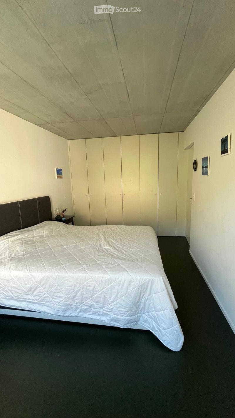 A neatly arranged bedroom with a single bed, white quilt, dark headboard, nightstand with a lamp, and a large built-in wardrobe.