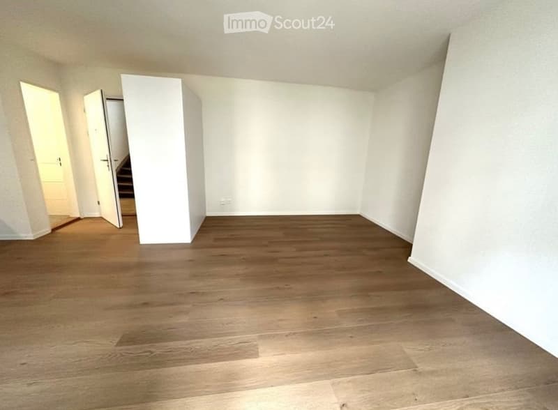 Empty room with wooden flooring and white walls, featuring an open doorway leading to another area.