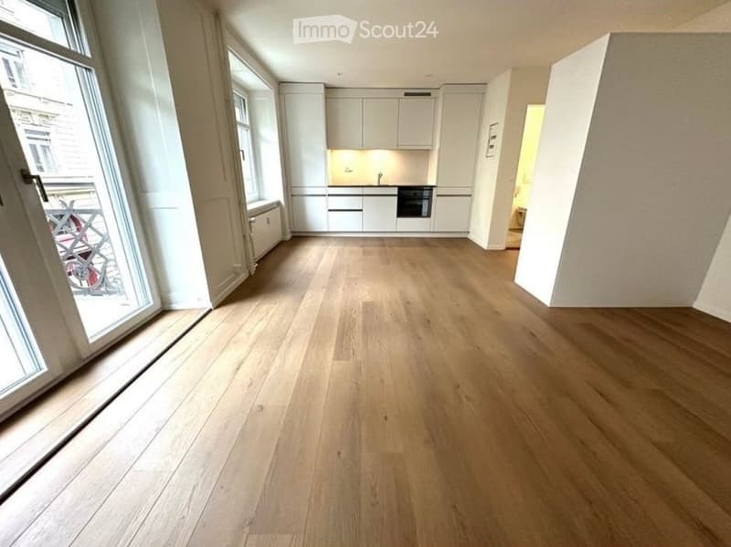 Empty room with light wooden flooring, white walls, large windows, and a view of a balcony area.