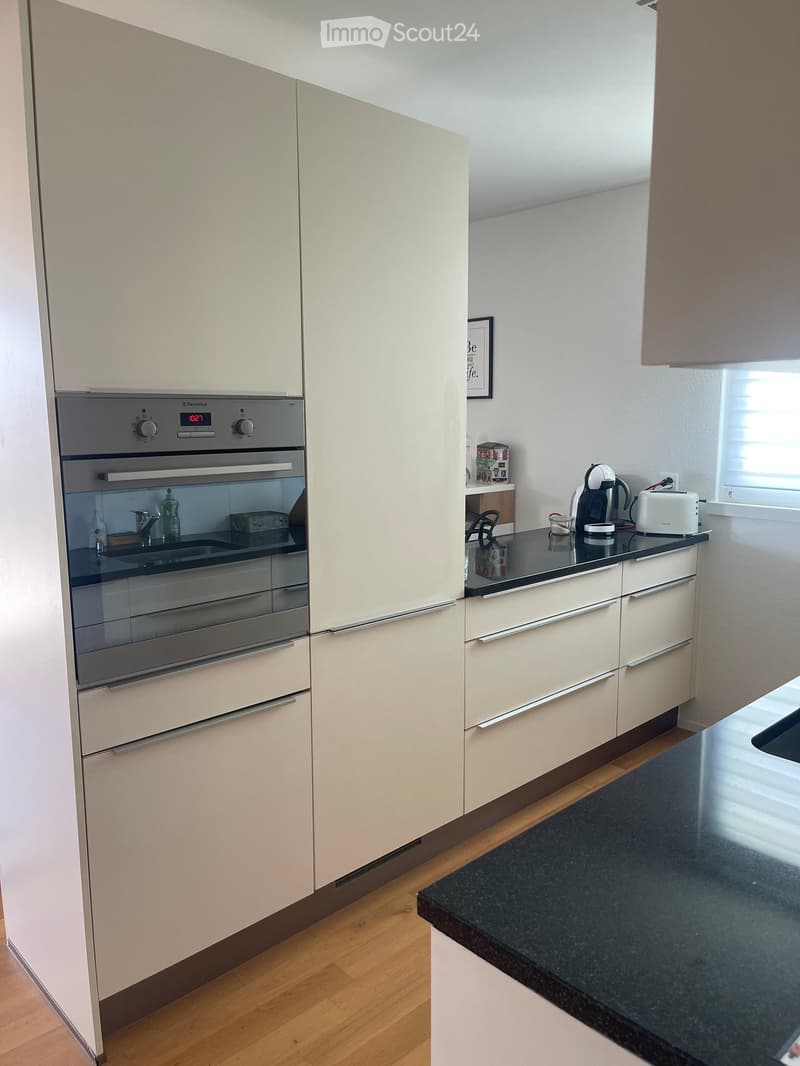 Modern kitchen with light-colored cabinets, stainless steel oven, granite countertop, and various appliances including a toaster and coffee maker.