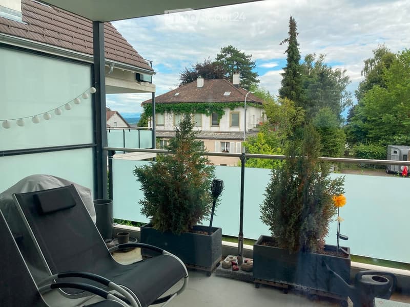 Balcony with lounge chair, potted plants, and a view of surrounding houses and greenery.